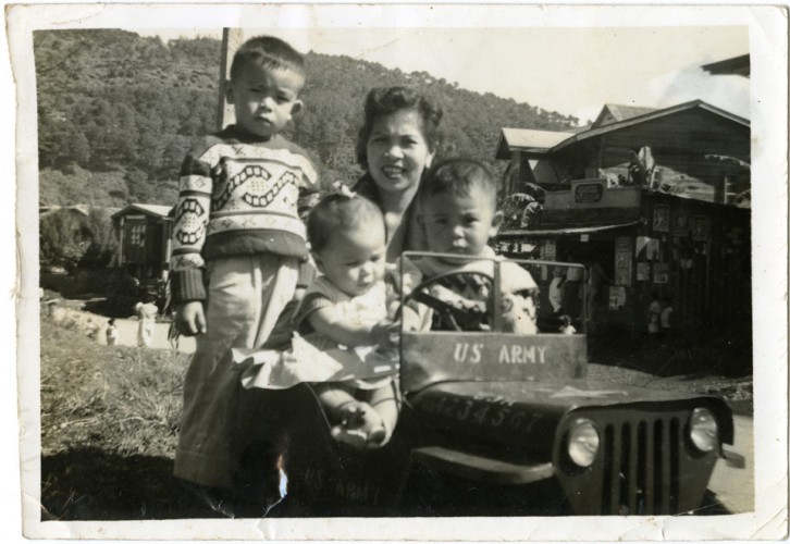 Josie Maxwell with her mother and brothers in a US Army toy car, 1959